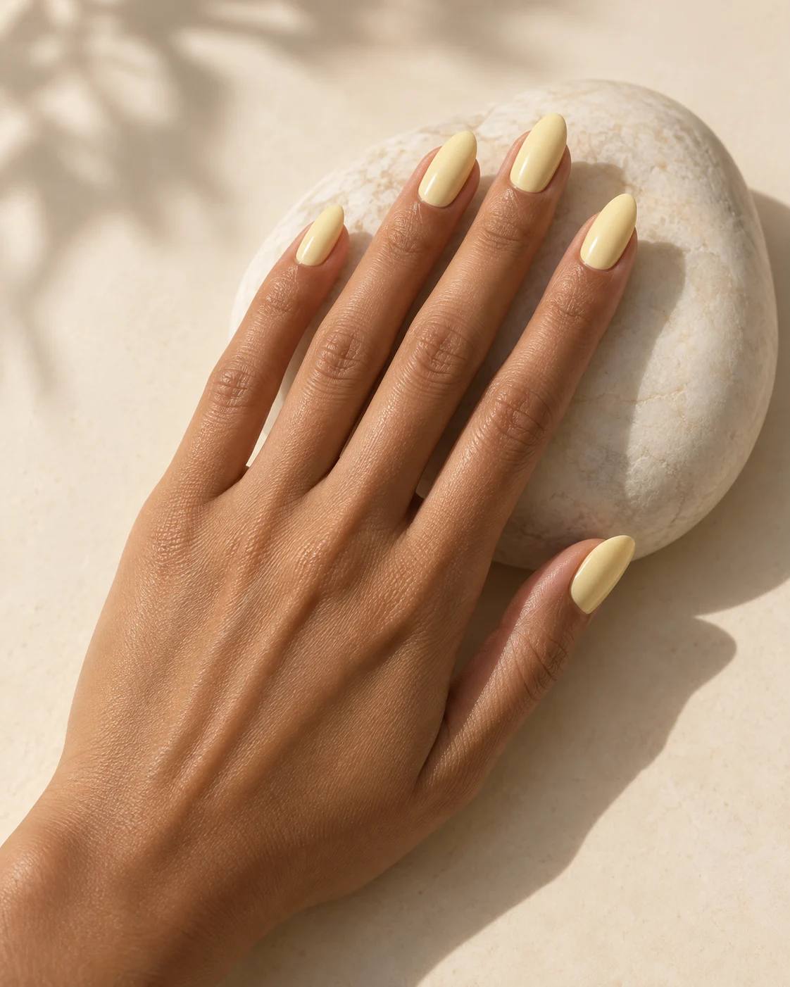Uñas almendradas de color amarillo mantequilla sobre una piedra clara.